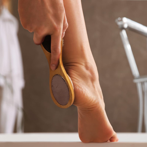 A wooden pedicure tool with a textured surface, being used on a bare foot.
