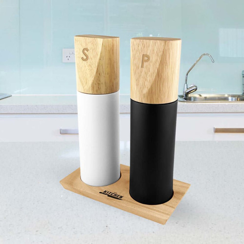 Two cylindrical grinders in white and black with wooden tops, sitting on a wooden base in a kitchen setting.