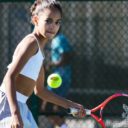 A tennis ball and a racquet in use on a court, featuring a young player in a white top and grey shorts.
