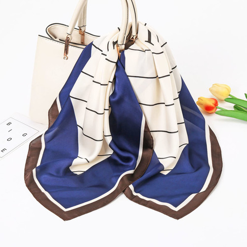 A silk chiffon scarf featuring a blue and cream geometric pattern, displayed draped over a handbag.