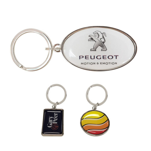 A collection of three keyrings, including a custom-shaped metal keyring with a logo, featuring silver and multicoloured designs.