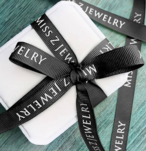 A white gift box wrapped with black ribbed fabric ribbon featuring a logo.