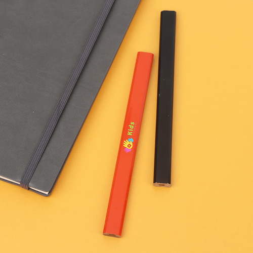 Two grey-lead pencils in red and black, placed next to a notebook on a yellow background.