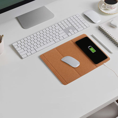 A cork wireless charger is placed on a desk alongside a white mouse, keyboard, and notebook.