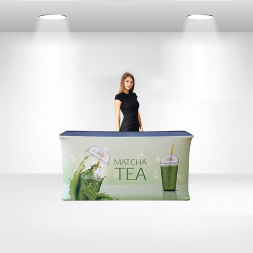 A folding fabric display counter with a green and blue design featuring matcha tea imagery, with a woman standing behind it.