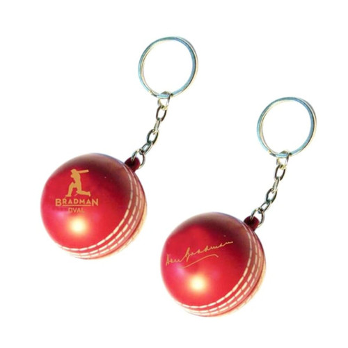 A red keyring featuring a cricket ball stress reliever, with a silver keychain and a logo.