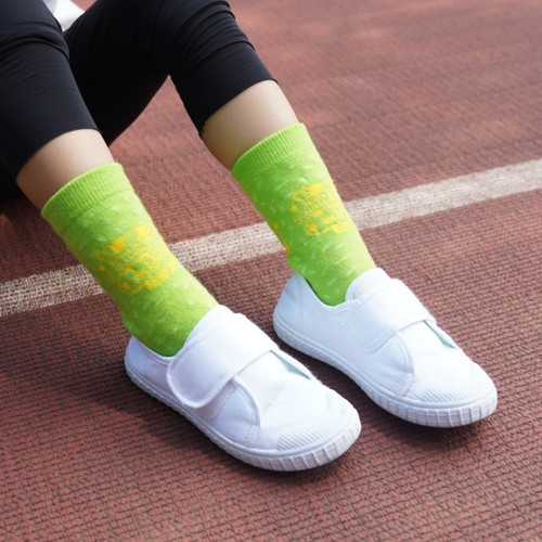 Bright green football socks with a towel bottom, worn with white slip-on shoes, against a textured surface.