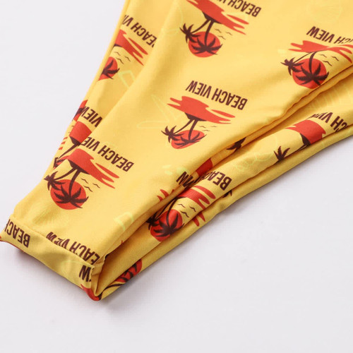 A yellow bikini bottom featuring palm tree and sunset graphics, with a logo present on the design.