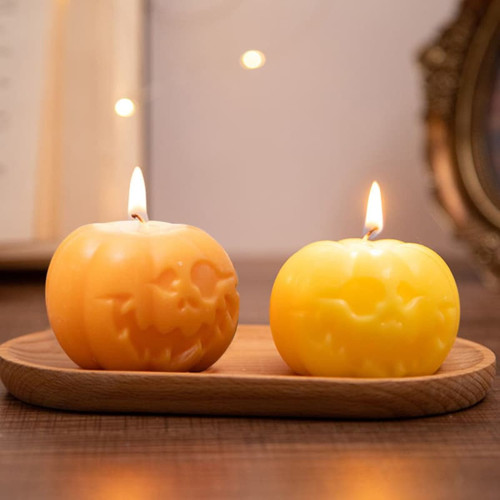 Two pumpkin-shaped candles in orange and yellow, featuring carved faces, displayed on a wooden tray.