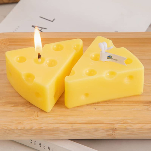 Triangle-shaped candles in yellow, resembling cheese, displayed on a wooden surface. One candle is lit.