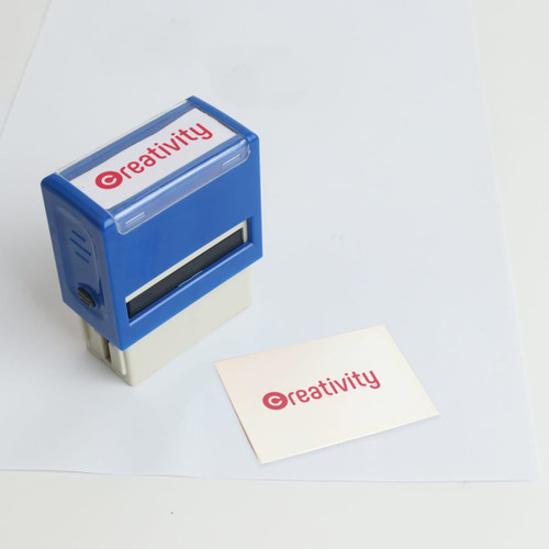 A self-inking rubber stamp in blue, positioned next to a blank card featuring a logo.