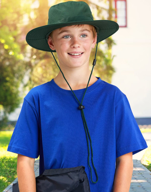 A boy wearing a green slouch hat with a break-away clip, paired with a blue t-shirt, smiles outdoors.