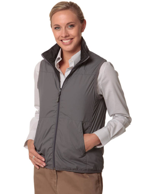 A woman in a grey versatile vest with a zip, paired with a striped shirt, smiling and standing with hands by her side.