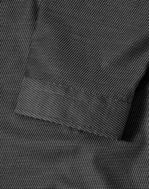 A close-up of a black pin dot stretch fabric with a 3/4 sleeve cuff of a button-up shirt. The shirt features a logo.