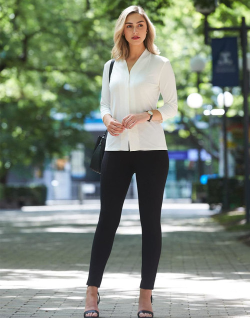 A model stands outdoors wearing black treggings and a white top, complemented by heels and a handbag.