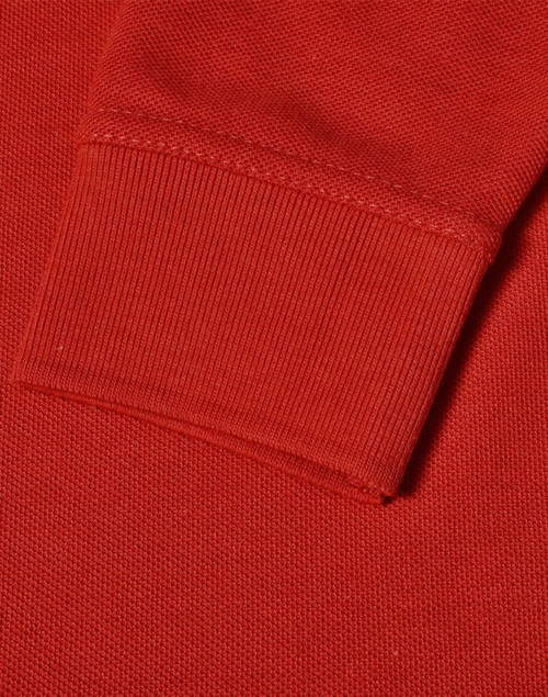 A close-up of a red long sleeve polo shirt, featuring a ribbed cuff and textured fabric.
