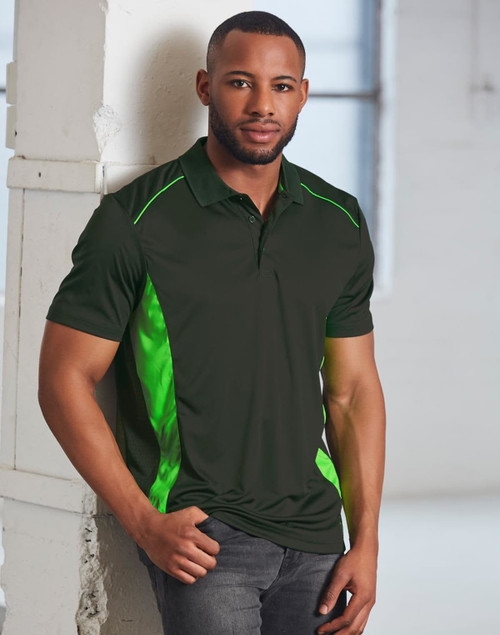 A man wears a dark green polo shirt featuring bright green contrast detailing and a logo. The background is a bright, industrial space.