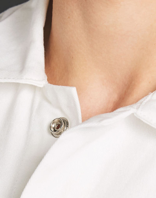 A close-up view of a white collared garment showing a button detail near the neckline. It has a logo.