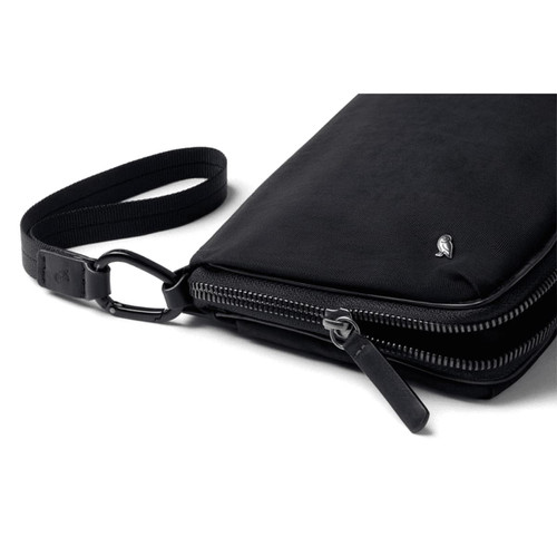 A black toiletry bag with a zippered closure and a detachable strap, featuring a discreet logo.