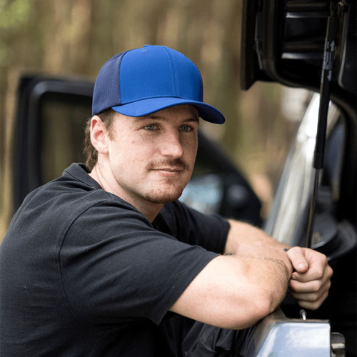 A blue and black cap with a logo, displayed on a person leaning against a vehicle.