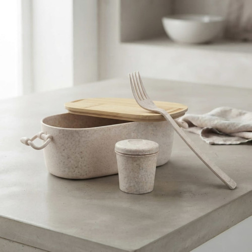 A bamboo lunch box in pale beige with a matching small container and a fork beside it, set on a concrete surface.