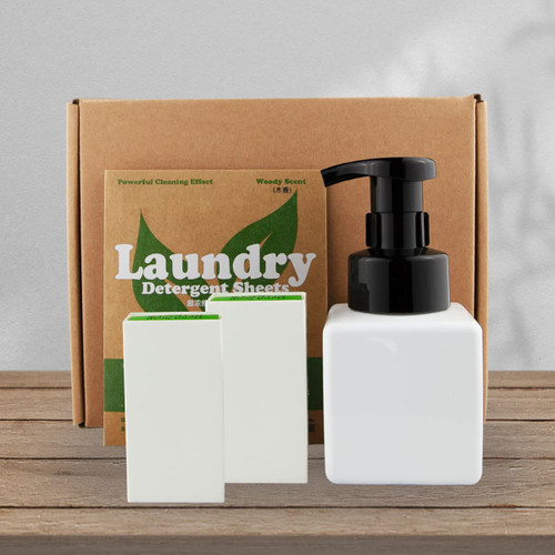 A white square pump bottle and two white laundry detergent sheets in a brown box with green accents.