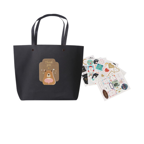 A black boutique paper bag with handles, accompanied by decorative stickers featuring various designs.
