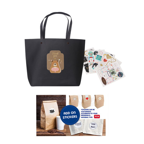 A black paper bag with handles, featuring a cute bear design, accompanied by assorted stickers.