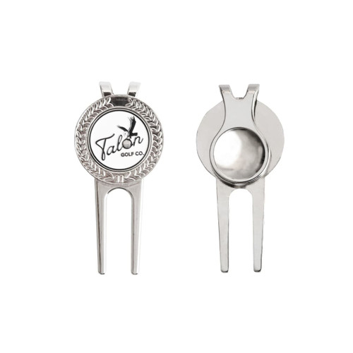 A silver golfers divot tool featuring a round ball marker with a logo. The tool has a pronged design for easy use.
