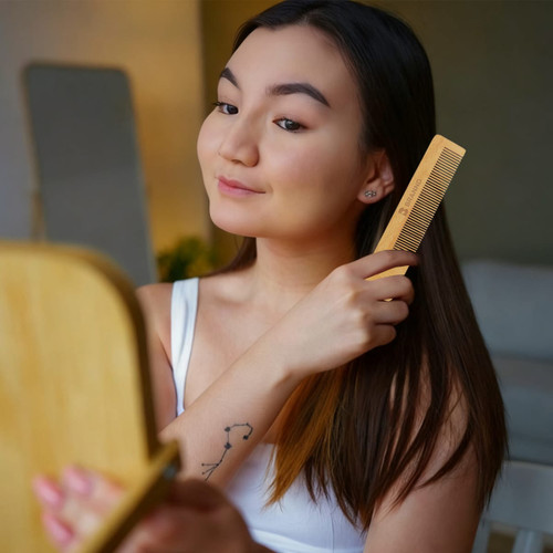 A beech wood comb in a person's hand, with long dark hair being styled in front of a mirror.