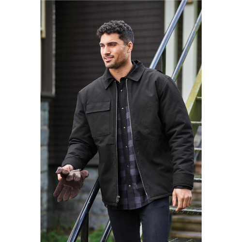 A black men's flatiron work jacket is worn by a man standing on stairs, holding gloves. The jacket features a pocket and has a casual style.