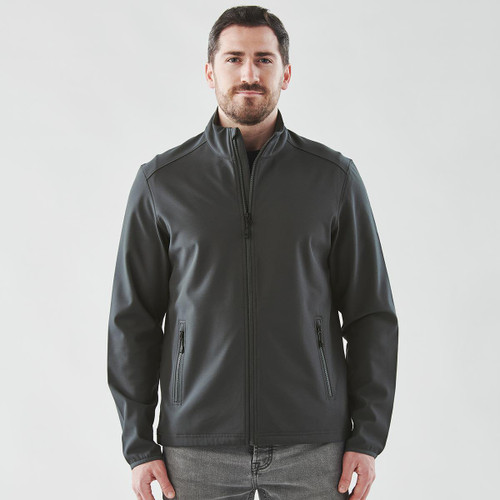 A man wearing a dark grey softshell jacket with a zip front and side pockets. The jacket has a logo.
