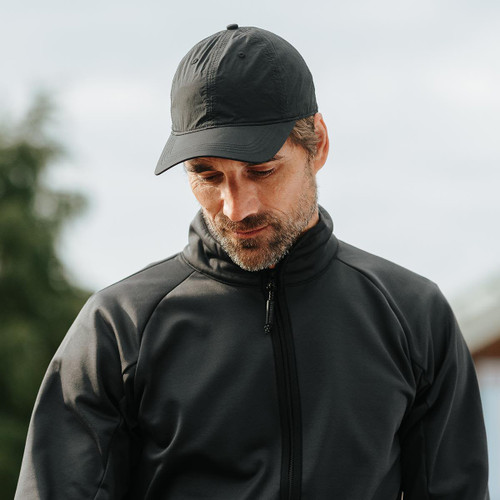 A black cap worn by a man in a black jacket, with a blurred outdoor background. The cap features a logo.
