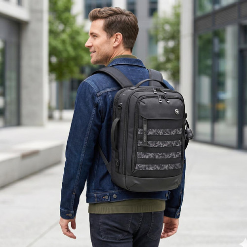 A man wearing a denim jacket carries a black Swissdigital Berg L Backpack with a patterned front in an urban setting.