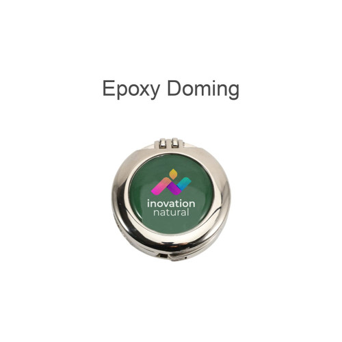 A round silver compact mirror with a green epoxy domed lid featuring a multicoloured logo and branding.