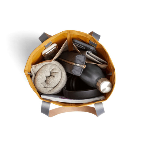 A yellow tote bag filled with a drink bottle, headphones, a blanket, a wallet, and a notebook. Includes branding.