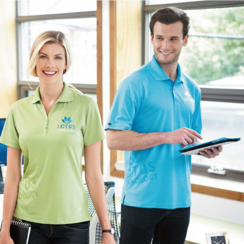 A green women's polo shirt and a blue men's polo shirt, both featuring a logo, displayed in a bright office setting.