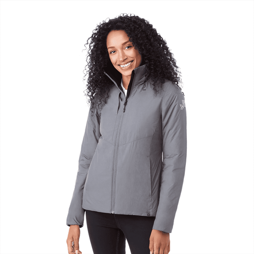 A woman wearing a grey insulated puffer jacket with a zip front and a logo on the sleeve.