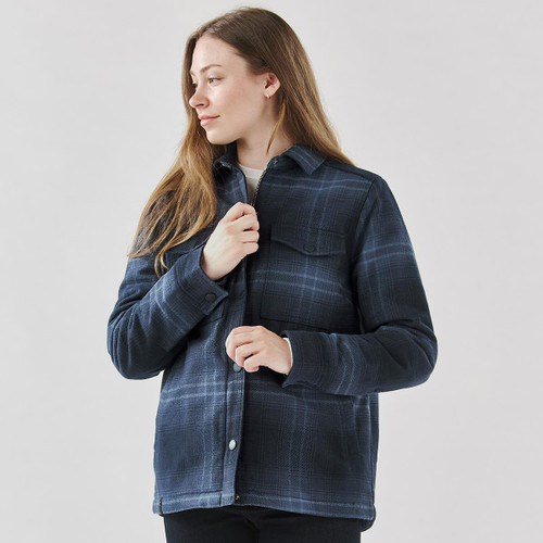 A woman wearing a navy plaid jacket with a Sherpa lining, featuring a button-up design and chest pocket.