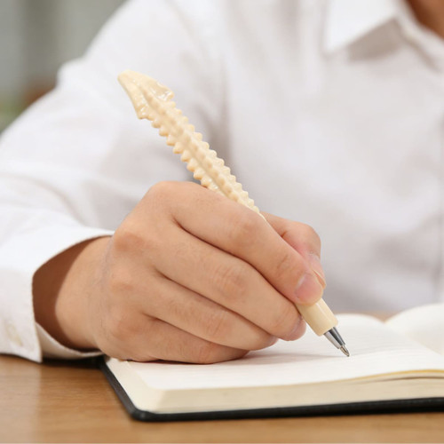 A spine-shaped pen in a person's hand, with a cream colour, resting on an open notebook.