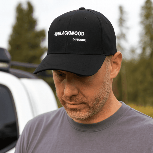 A black strapback baseball cap with a logo, worn by a person outdoors near a vehicle.