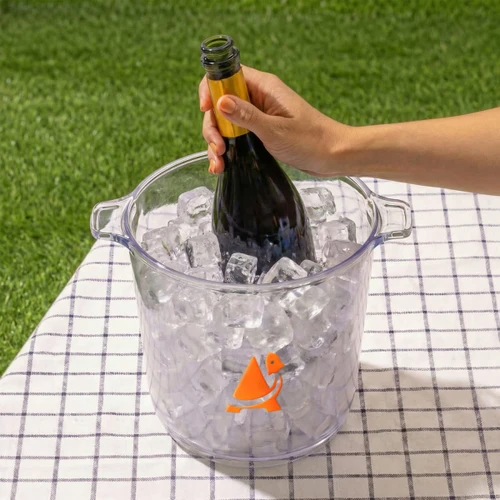 A clear ice bucket filled with ice, holding a bottle of sparkling wine, featuring an orange logo.