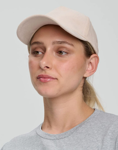 A beige Jacquard Texture 5 Panel Cap worn by a woman, featuring a curved brim and a minimalist design.
