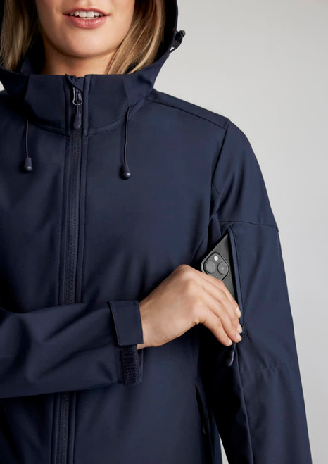 A woman wearing a navy jacket with a zippered pocket on the sleeve, featuring a logo on the jacket.
