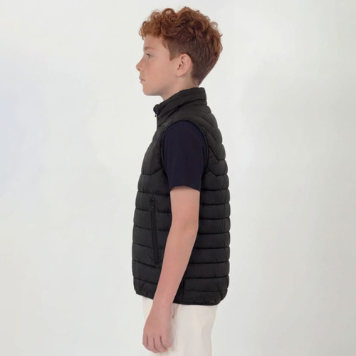 A youth black puffer vest displayed on a child from the side, featuring a high collar and a simple design.