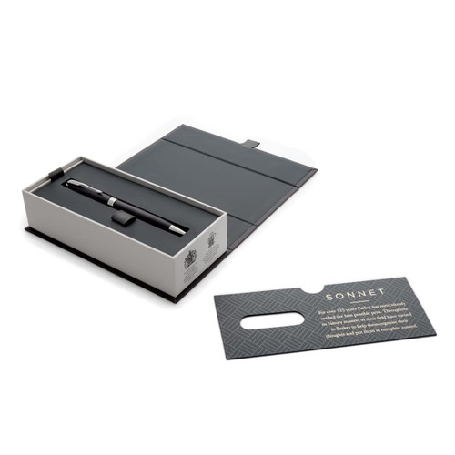 A matte black ballpoint pen inside a grey box with a card nearby, featuring a logo and elegant design.