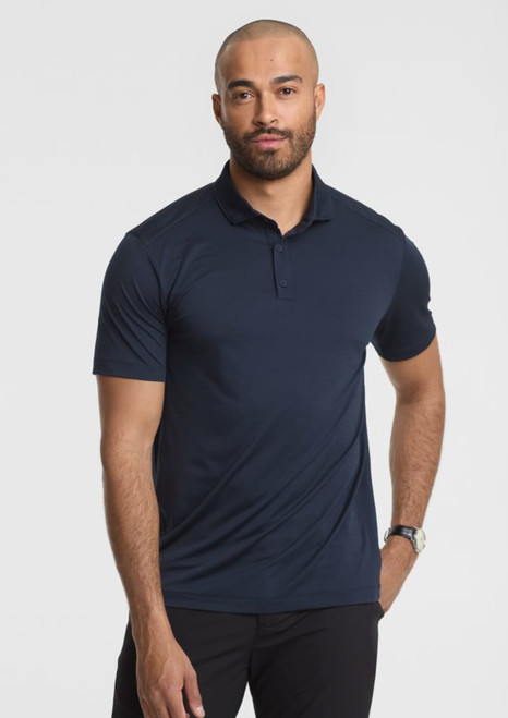 A man stands wearing a navy blue short sleeve polo shirt, featuring a collar and a logo.