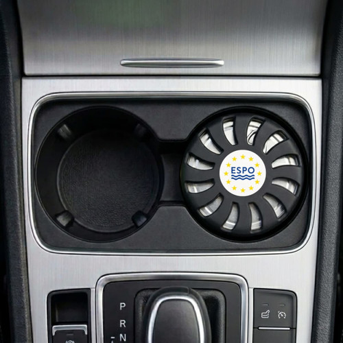 An air freshener in a circular black holder, placed in a car cup holder, featuring a logo.