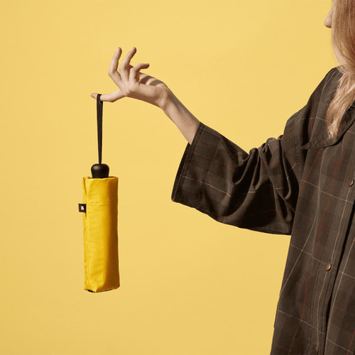 A yellow compact umbrella held by a person, with a plain background and a visible logo on the umbrella.