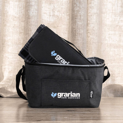 A grey insulated bag with a black picnic blanket folded inside, featuring a logo on the bag.